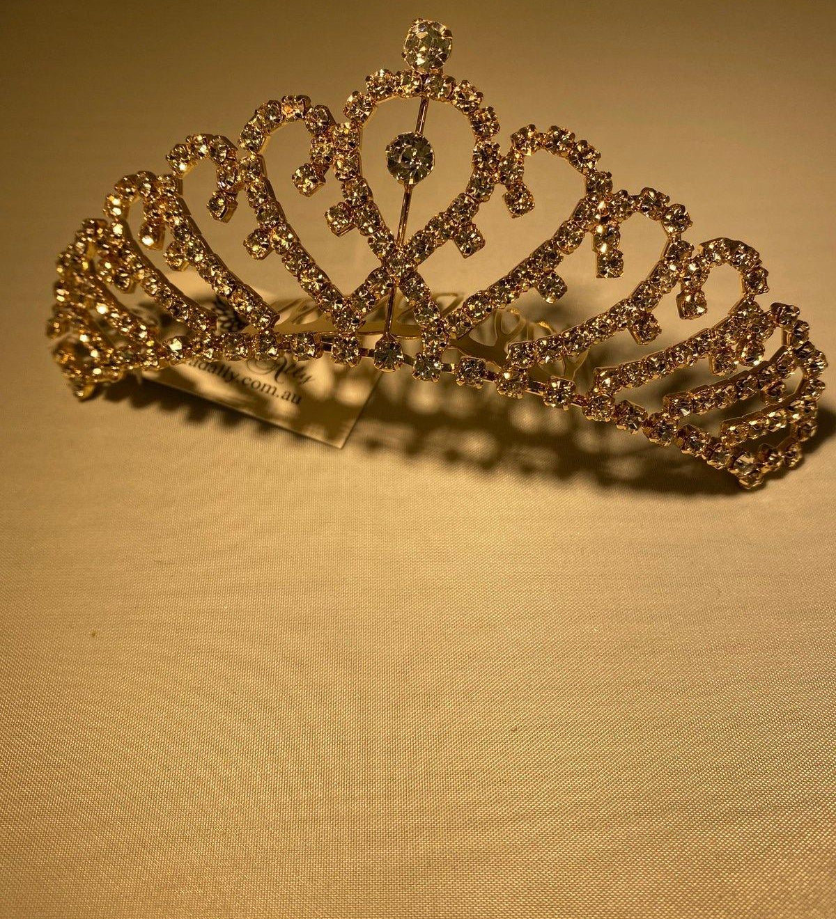 This gold tiara with overlapping heart design and sparkling crystals makes it a stunning accessory to any attire, with slide comb attached.
