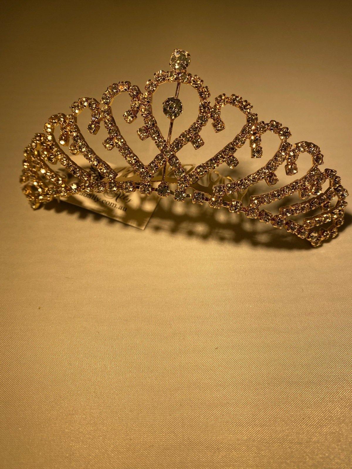 This gold tiara with overlapping heart design and sparkling crystals makes it a stunning accessory to any attire, with slide comb attached.